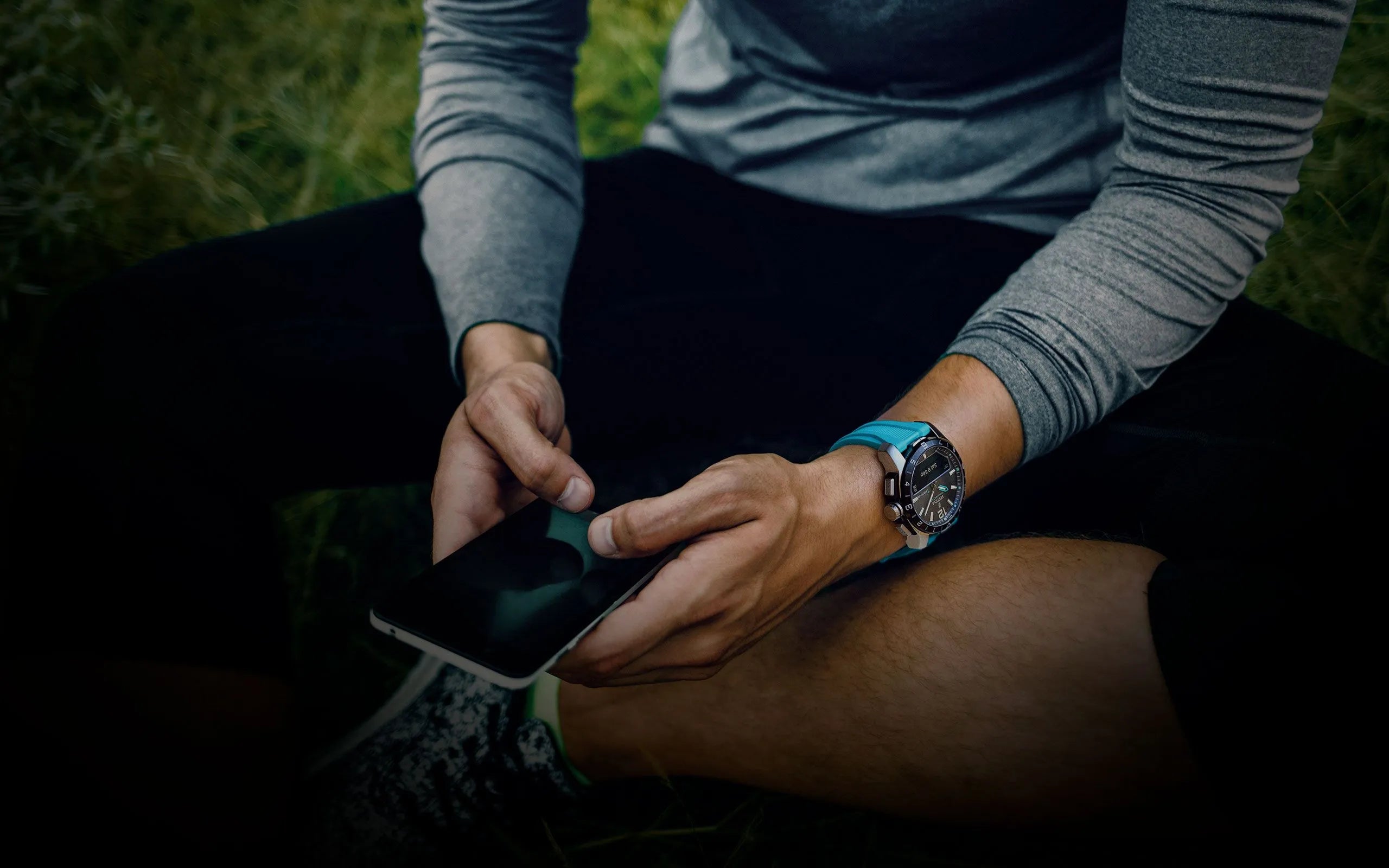 En person iført et Festina Connected D ur med en blå rem, set mens han sidder udendørs og betjener en smartphone. Uret kombinerer et sporty design med moderne teknologi, ideelt til en aktiv livsstil.