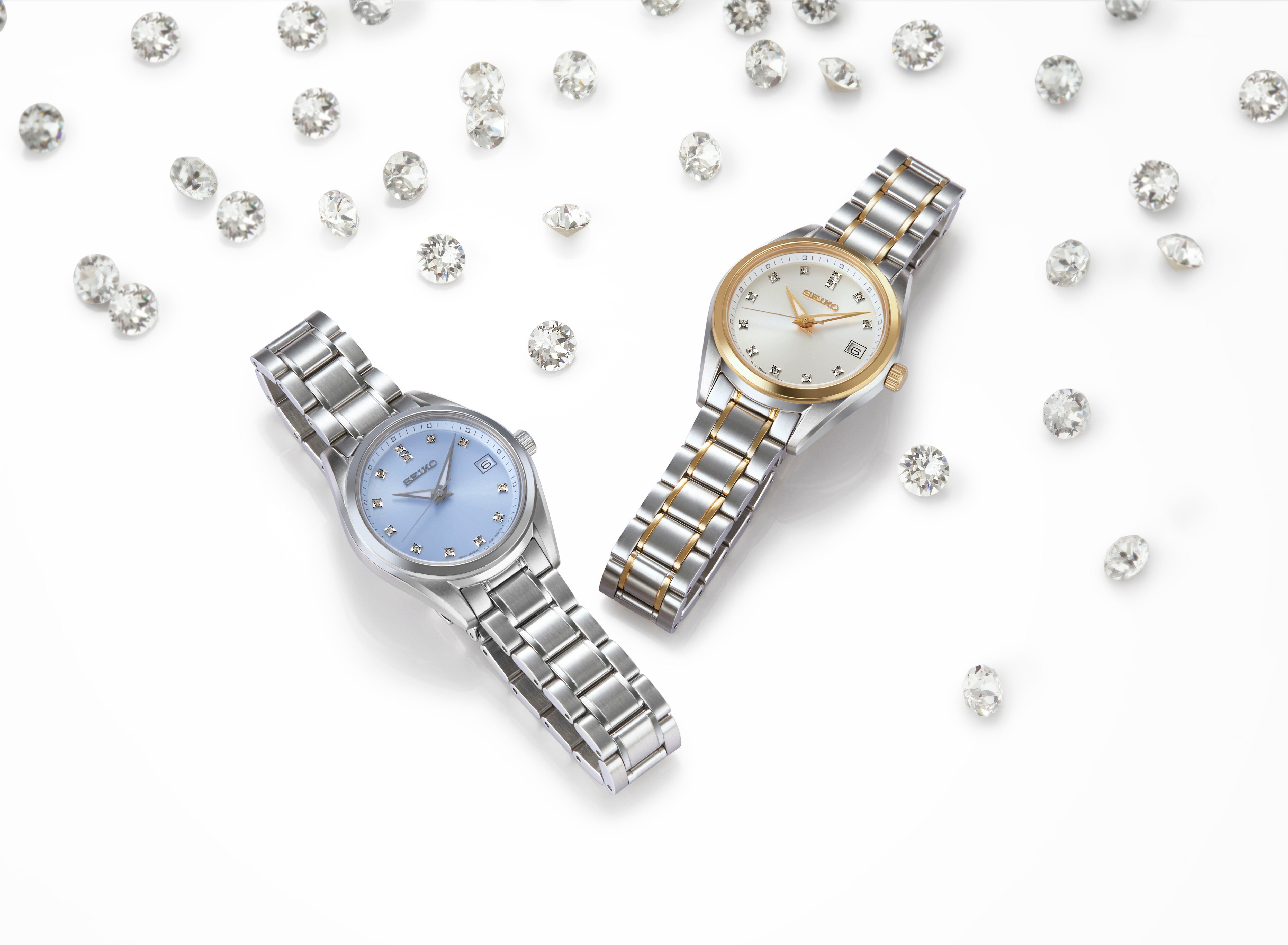 To Seiko ure, SUR581P1 i sølv og SUR582P1 i guld/sølv, præsenteres på en hvid baggrund omgivet af løst spredte, skinnende diamanter.