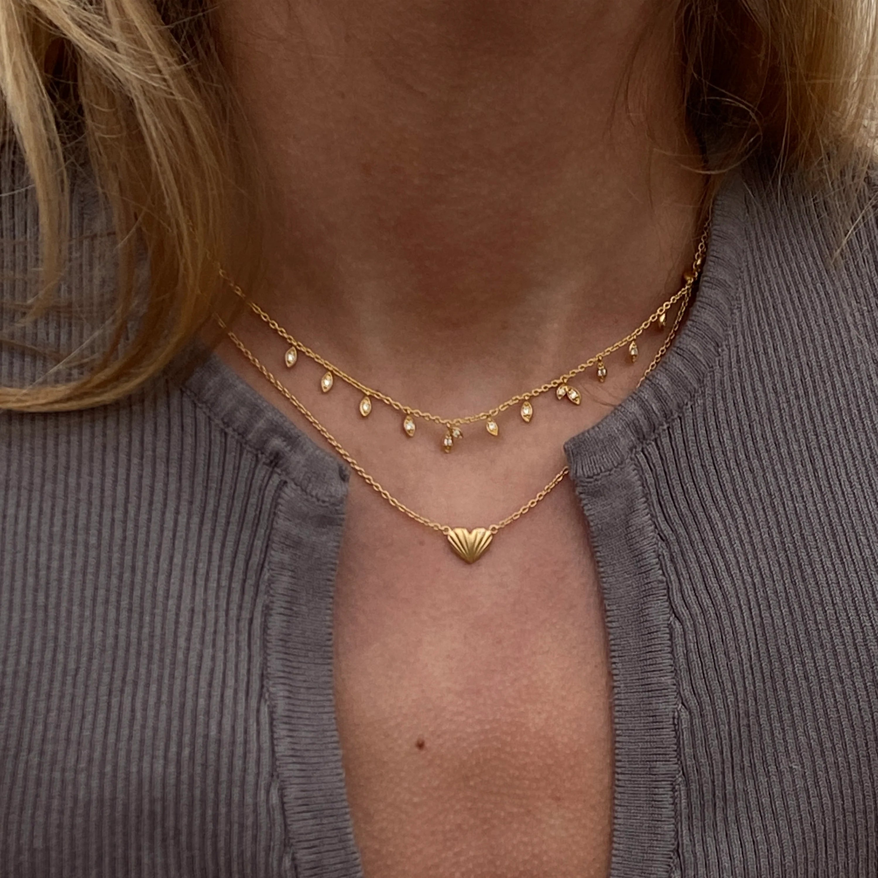 To elegante ByBiehl halskæder i forgyldt sølv, båret sammen for et sofistikeret og stilfuldt look. Den ene halskæde har små vedhæng, der fanger lyset, mens den anden har et smukt, minimalistisk hjertevedhæng. Perfekt til enhver lejlighed.