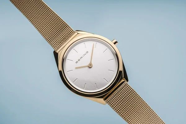 Et Bering dameur, model 17031-334, med en ultra tynd profil og poleret guldfinish. Uret har en minimalistisk hvid urskive og en matchende guldfarvet mesh-rem.