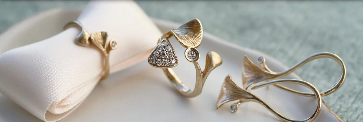 Banner med guldsmykker i organisk design og brillanter placeret på lys stofrulle og blød, elegant baggrund.