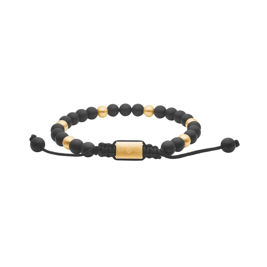 SON of NOA herrearmbånd med matte sorte agatsten på 6 mm, guldfarvede detaljer i rustfrit stål med IP gold-belægning, justerbar nylonlukning og længde fra 19 til 25 cm. Et maskulint stenarmbånd i sort og guld.